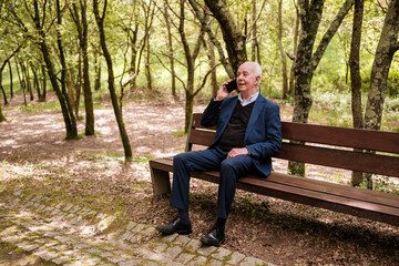 Fototapeta premium Senior businessman talking on smartphone sitting on park bench