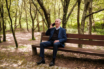 Fototapeta premium Senior man talking on cell phone on park bench