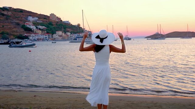A travel woman in a white summer dress looks at the village of Vourkari, Kea island, Cyclades, Greece, during sunset time