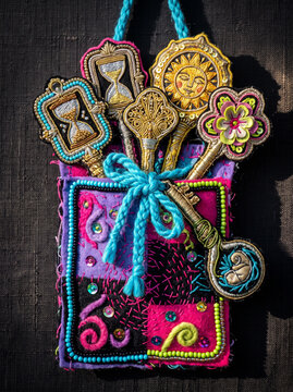 Vertical photo of a handmade embroidered talisman pouch. Colorful textile amulet with stitched key, hourglass, sun and flower symbols
