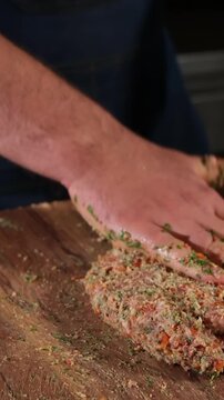 Professional cook mixing seasoned ground meat with fresh herbs on a wooden board