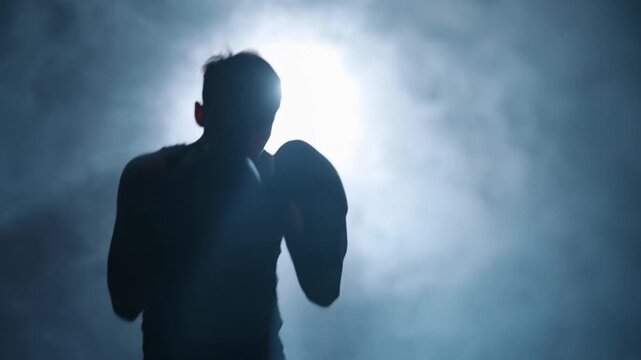 Silhouette of Boxer Shadow Boxing in Smoky Dark Studio with Backlight