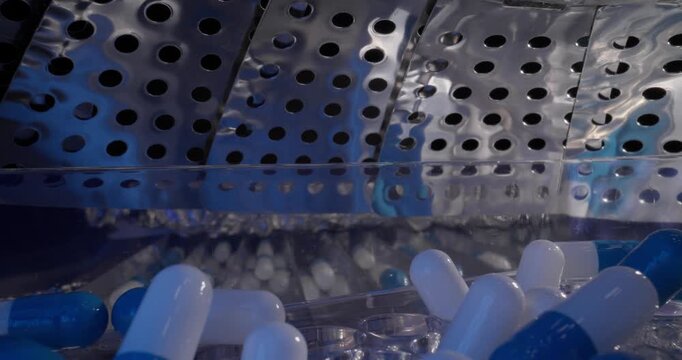 Slow motion close up of blue and white capsules tumbling inside stainless steel hopper in pharmaceutical production, probe macro view.