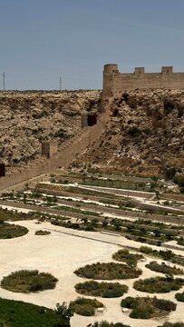 Long medieval fortress walls climbing up rocky mountain ridge over green park terraces, Almeria, Spain
