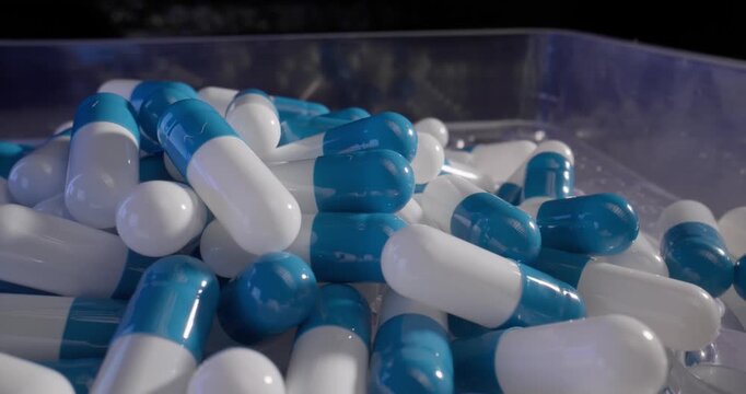 Slow motion blue and white capsules tumbling and piling inside clear plastic tray on production table in laboratory, probe macro view.