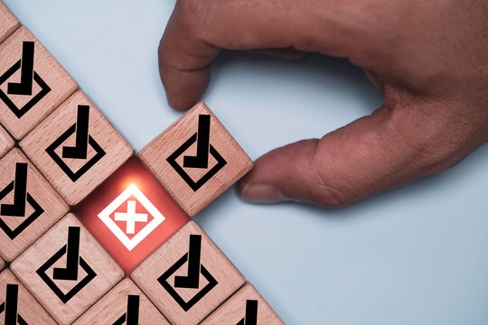 Hand selects a check mark block beside a glowing cross mark among approved choices symbolizing rejection, error detection, quality control, decision making, evaluation and risk management process.