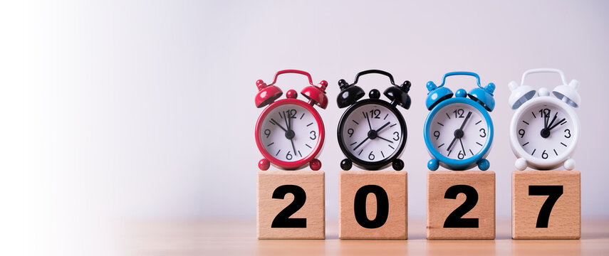 2027 time planning concept with colorful alarm clocks on wooden number blocks symbolizing new year countdown, deadlines schedules, time management and preparation for future goals and priorities.