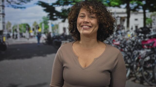Smiling woman beckons with bare hand on bustling street lined with parked bicycles by rack; invitation.