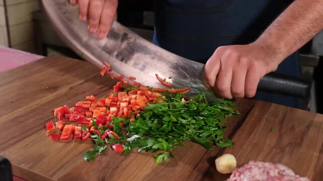 Close-up of a professional chef chopping fresh red peppers and parsley on a wooden cutting board