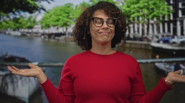 Woman with curly hair holds both hands out by canal on street in amsterdam with eyes closed; quiet doubt.