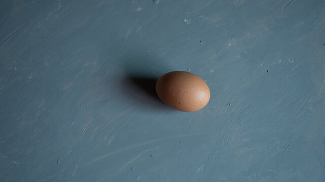 Fresh brown raw chicken egg on blue textured surface