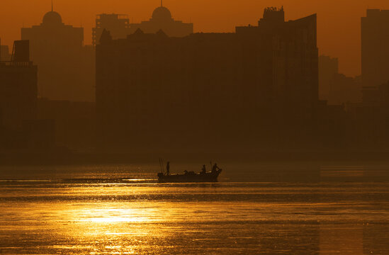 A backlit image of fishermen fishing at Tubli bay during sunrise with highrise building at the backdrop, Bahrain