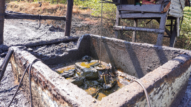 Long steel pipe extracting crude oil with dynamic water splash at historic Wonocolo traditional well, Bojonegoro, East Java, Indonesia. Authentic artisanal petroleum mining and energy production.