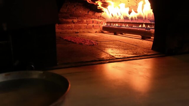 Professional chef placing a long Turkish Pide into a hot, flaming stone oven with a wooden peel