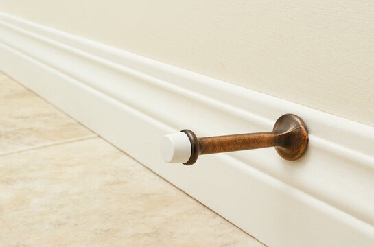 Wall mounted door stopper on white baseboard used for preventing door impact.