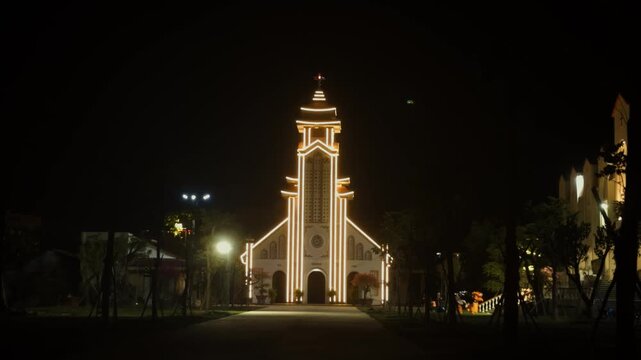Da nang pink church illuminated at night, warm yellow lights outlining the ornate facade and bell tower, a historic catholic landmark and serene cultural symbol in vietnam
