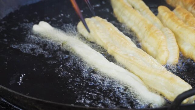 Close-Up of Dough Sticks Frying in Hot Oil with Chopsticks