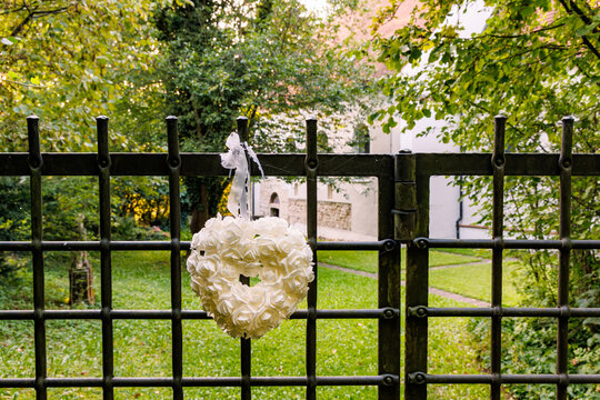 White rose heart wreath hanging on wrought iron gate in garden near historic building, romantic wedding celebration and love concept