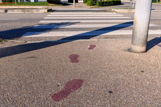 Red painted footprints on sidewalk leading towards pedestrian crosswalk, road safety and urban pedestrian guidance concept