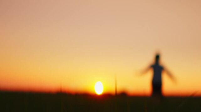 Joyful child running through open field at golden sunset, arms outstretched in freedom, silhouetted against warm glowing sky and peaceful natural horizon