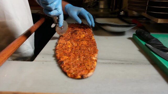 Restaurant chef cutting traditional Turkish lahmacun pide on a marble countertop with a pizza cutter
