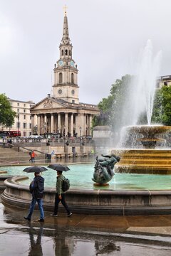 LONDON, UK - JULY 9, 2024: People visit Trafalgar Square on a rainy summer day in London. The square is a part of the City of Westminster and was constructed in 1840s.