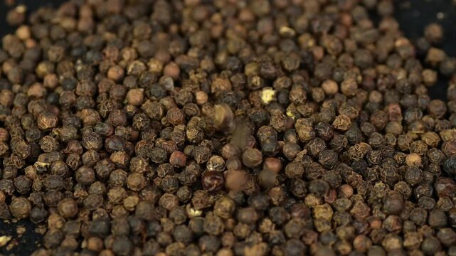 Black pepper. Peppercorns falling on a table, close-up, slow motion