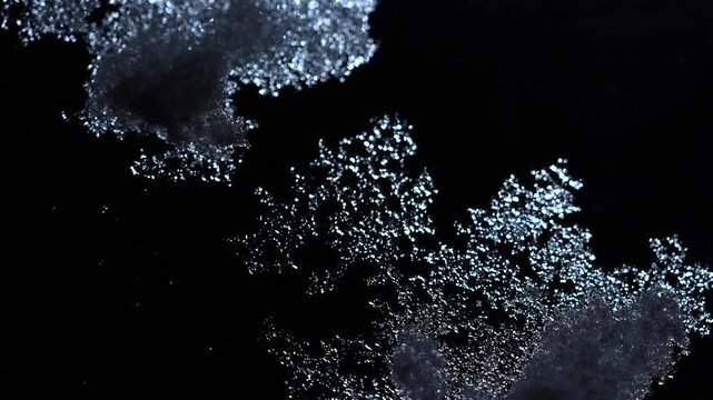 Close up of snow patterns on a glass surface, creating a sparkling effect against the darkness.