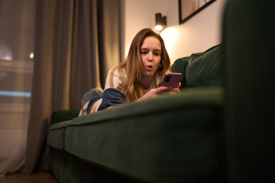 Surprised woman reacting to smartphone content while lying on sofa