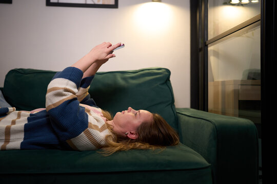 Relaxed woman lying on couch using smartphone under soft light