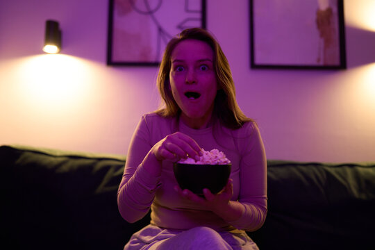 Female sitting on sofa eating popcorn under colorful lighting