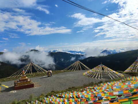 Colorful Tibetan Prayer Flag Cones and Dense Prayer Flags at Mountain Summit with Dramatic Sea of Clouds and Mountain Ranges in Western Sichuan China