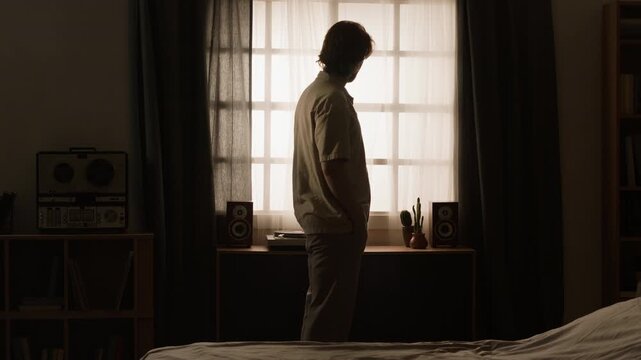 Caucasian young adult man pacing slowly with head down in front of window, feeling depressed. Suitable for mental health awareness campaigns, therapy ads, or wellness content