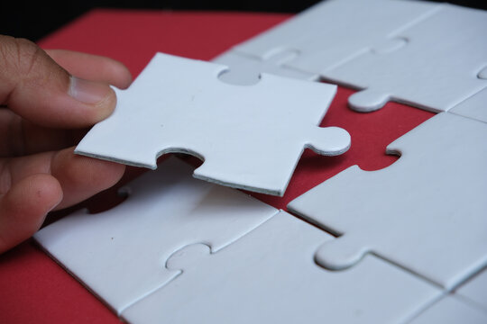 A hand attempts to fit in a missing puzzle piece, symbolizing alliance, unity, teamwork, solutions, success, and problem-solving. It serves as a metaphor for business integration or the challenge of a
