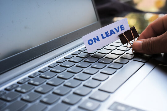 A hand placing an "ON LEAVE" sign on a keyboard. Concept of taking a break from work, annual leave, holidays, or family time.