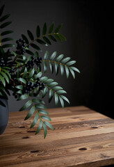 Obraz premium Minimalist interior decor, botanical arrangement with dark berries and green leaves on a rustic wooden table in a moody home office or living room space