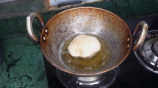 Close up of a puri or poori or luchi dough getting deep fried in aluminum frying pan with hot oil. Cooking poori or luchi on the gas stove at home kitchen.