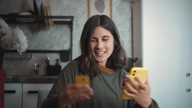Young Latina woman shopping online at home, then looking at the camera while holding a shopping bag after completing her purchase.
