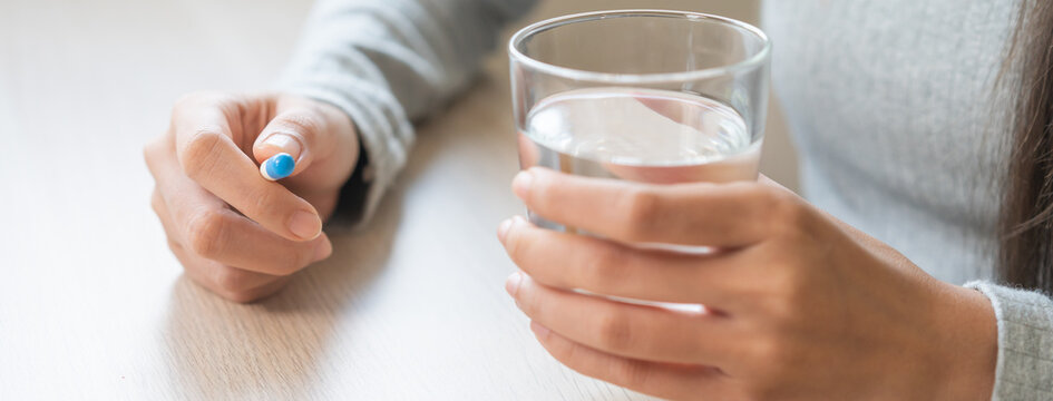 Sick, asian young woman, girl hand holding pill capsule, painkiller medicine from stomach pain, head ache, pain for treatment, take drug or vitamin and glass of water at home, pharmacy and health care