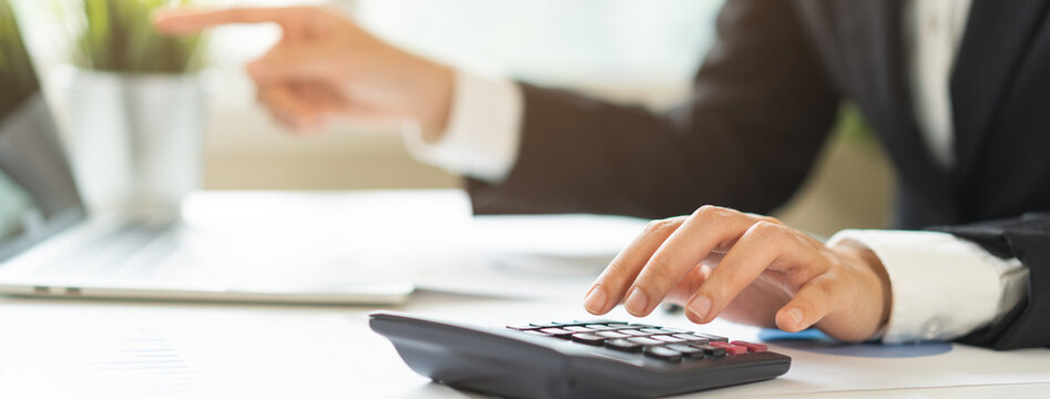 Business woman accountant using calculator, pointing at laptop screenwhile working on financial report, analyzing corporate data or presenting budget analysis in office workspace.