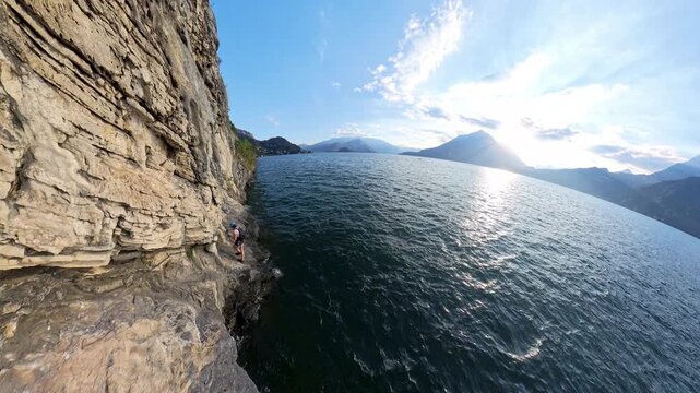 Wide angle view of a female climber traversing Via Ferrata Morcate on Lake Como cliff at sunset, Italy
