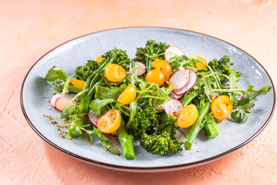 Grilled green spring vegetables: radish, tomato, broccolini on stone background.