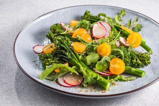 Grilled green spring vegetables: radish, tomato, broccolini on stone background.
