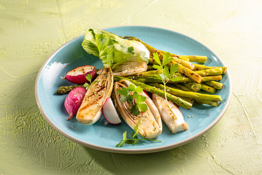 Braised chicory endives, asparagus, radish on a light stone background. Traditional Belgian cuisine.