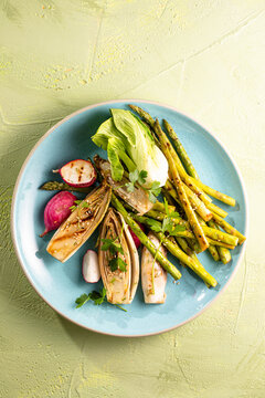 Braised chicory endives, asparagus, radish on a light stone background. Traditional Belgian cuisine.