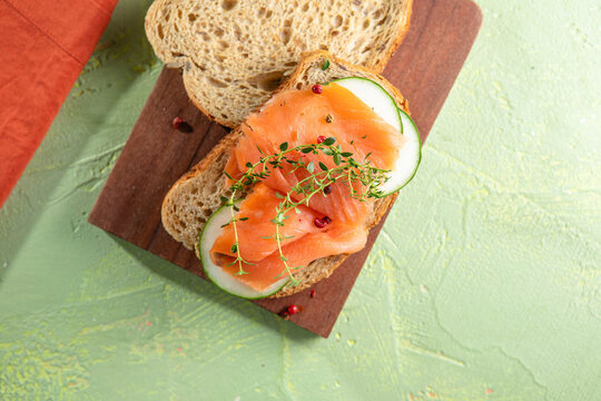 Rye bread sandwich with salted salmon, cucumber, greens on wooden cutting board closeup