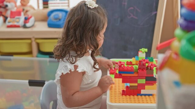 Girl stacking colorful toy blocks with right hand at a play table in a building; curiosity creative play.