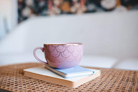 Pink mug staying on notebooks at rattan table close up