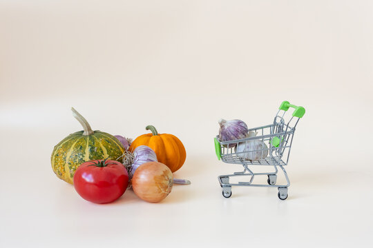 Fresh vegetables and shopping cart with groceries on beige background with copy space