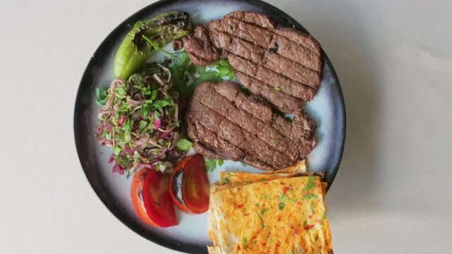Plate with grilled beef steak, fresh salad, tomatoes, pepper, and flatbread rotating top view